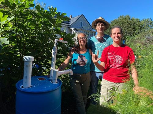 three people standing near a big blue barrel